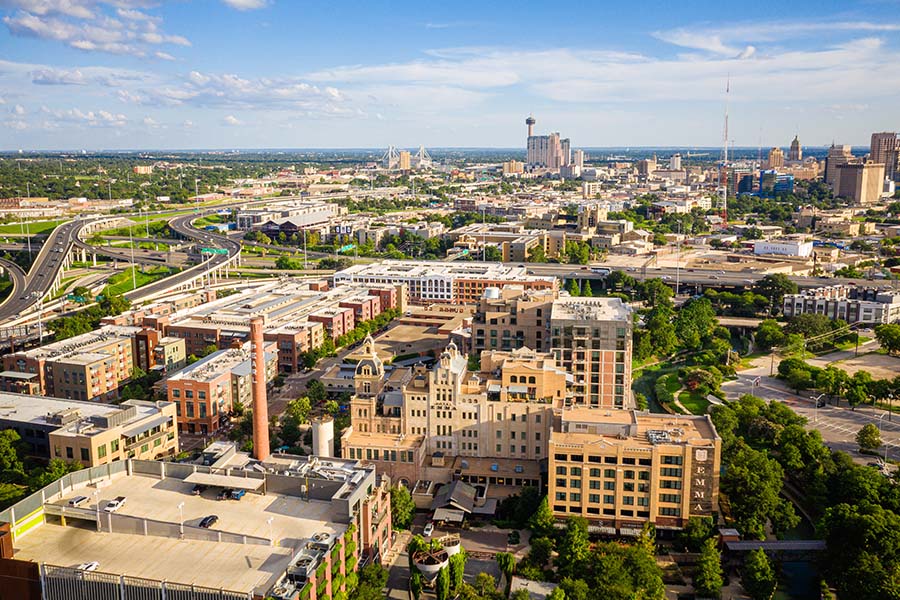 Contact - Aerial of Pearl District San Antonio Texas Displaying Multiple Buildings, a Bridge, and Trees on a Bright Day